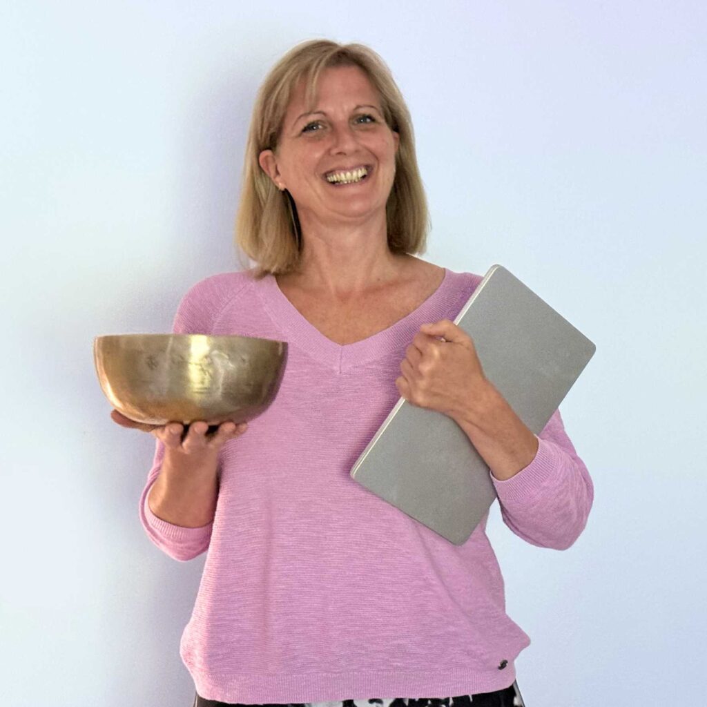 Smiling woman in a pink sweater holds a large bronze trophy bowl in one hand and a gray binder in the other against a pale blue wall.